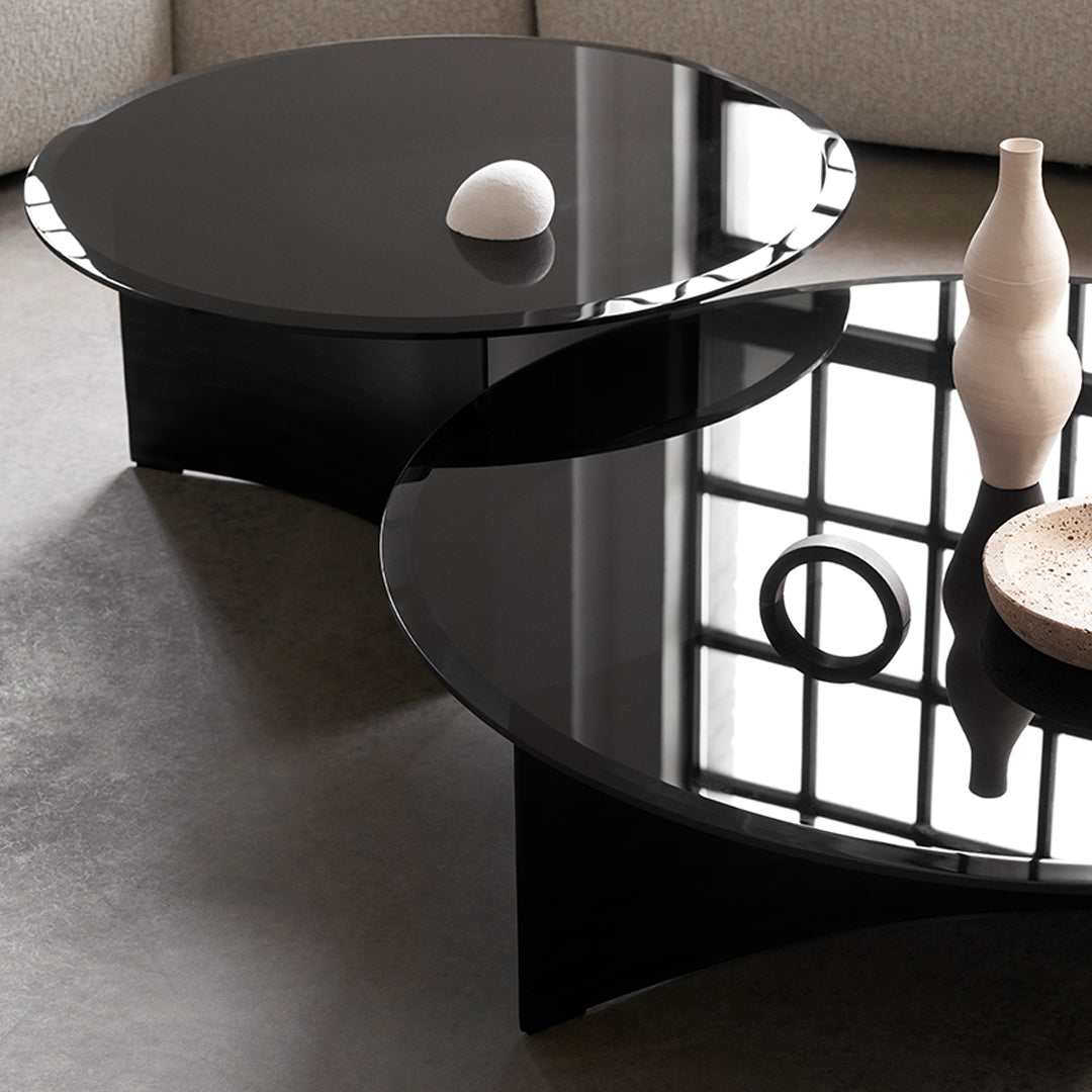 Black circular coffee tables with glossy surfaces, featuring sleek, modern designs against a neutral backdrop.