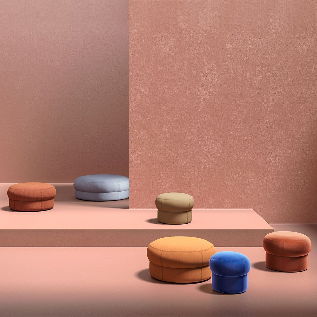 Colorful poufs in terracotta, blue, green, yellow, and orange against a soft pink backdrop, showcasing modern design.