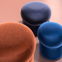 Colorful velvet ottomans in orange, dark blue, and light blue with smooth, rounded shapes on a soft background.