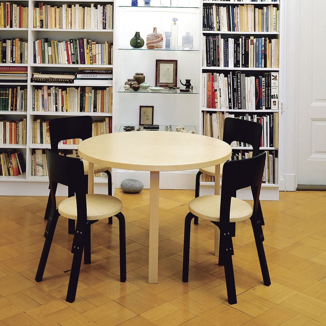 Light wood round table with four black and light brown chairs in a cozy, book-filled setting. Perfect minimalist design.