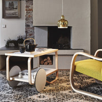 Stylish wooden cart with a natural finish, featuring a white shelf and round wheels, set against a patterned dark rug.