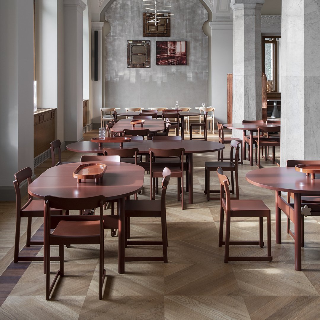 Round wooden tables and chairs in rich maroon hues, set against light gray and patterned flooring.
