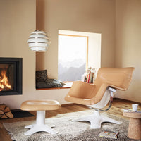 Tan leather chair and ottoman with white base, set against a neutral wall and patterned rug in cozy setting.