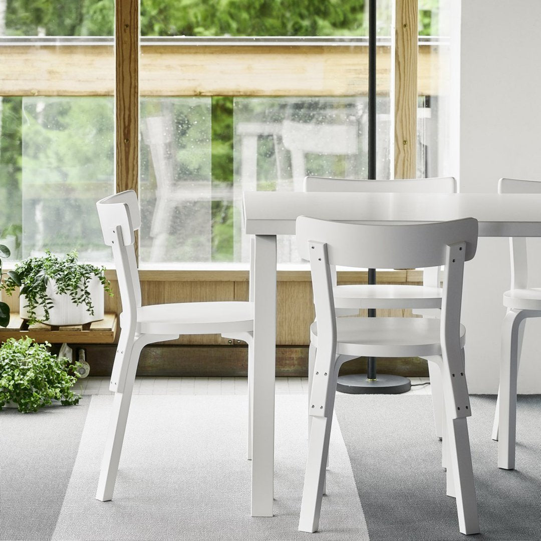 White wooden chairs with a sleek design, placed on a light grey carpet, against a backdrop of greenery.