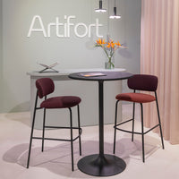 "Stylish maroon bar stools and sleek black table against a soft green backdrop, accented with vibrant orange flowers."