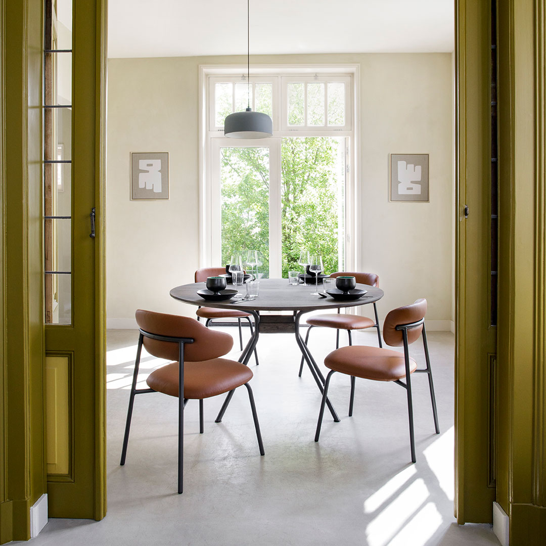 Round black dining table with modern black chairs and warm terracotta upholstered seats in a bright, light-filled room.