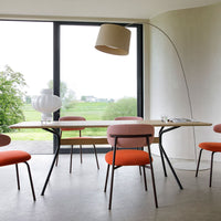 Modern dining room with orange and pink chairs, light wooden table, and a beige lamp against a minimalist backdrop.
