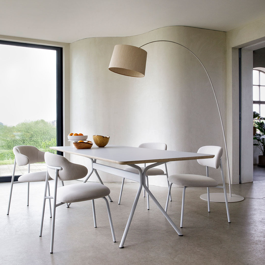 Modern white dining table with matching chairs, soft beige lamp, and minimalist decor in a light, neutral-toned space.