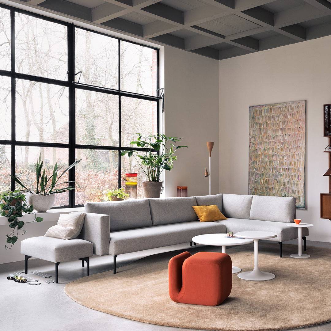 Modern gray sectional sofa with pastel accents, featuring a circular beige rug and bold red and yellow decor elements.