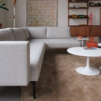 Light gray sectional sofa on brown carpet with white circular coffee table and colorful wall art in the background.