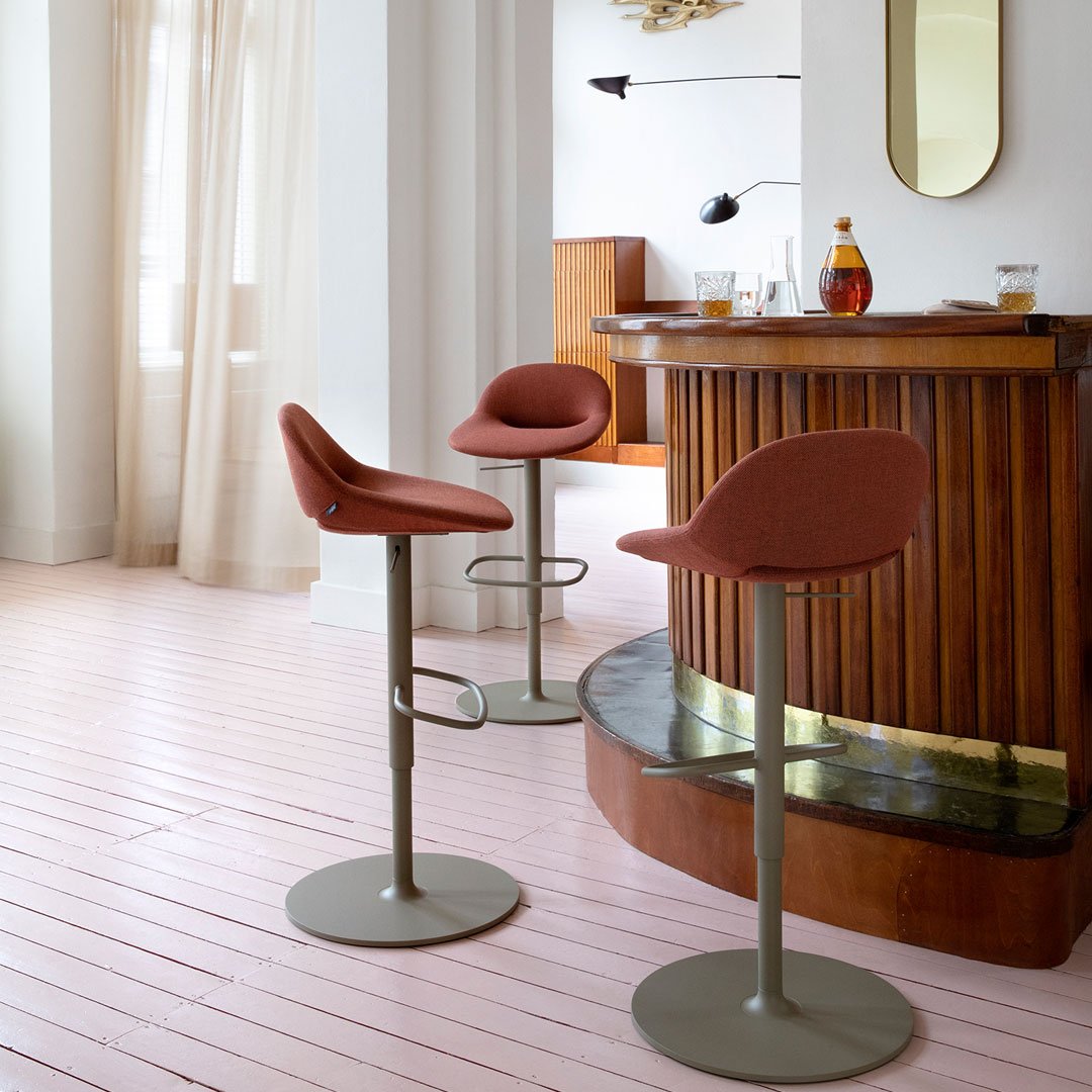 Two modern bar stools with rust-colored seats and muted green bases, complementing a contemporary wood bar setup.