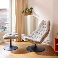 Light gray tufted fabric lounge chair with matching ottoman on a sleek black base in a bright interior setting.