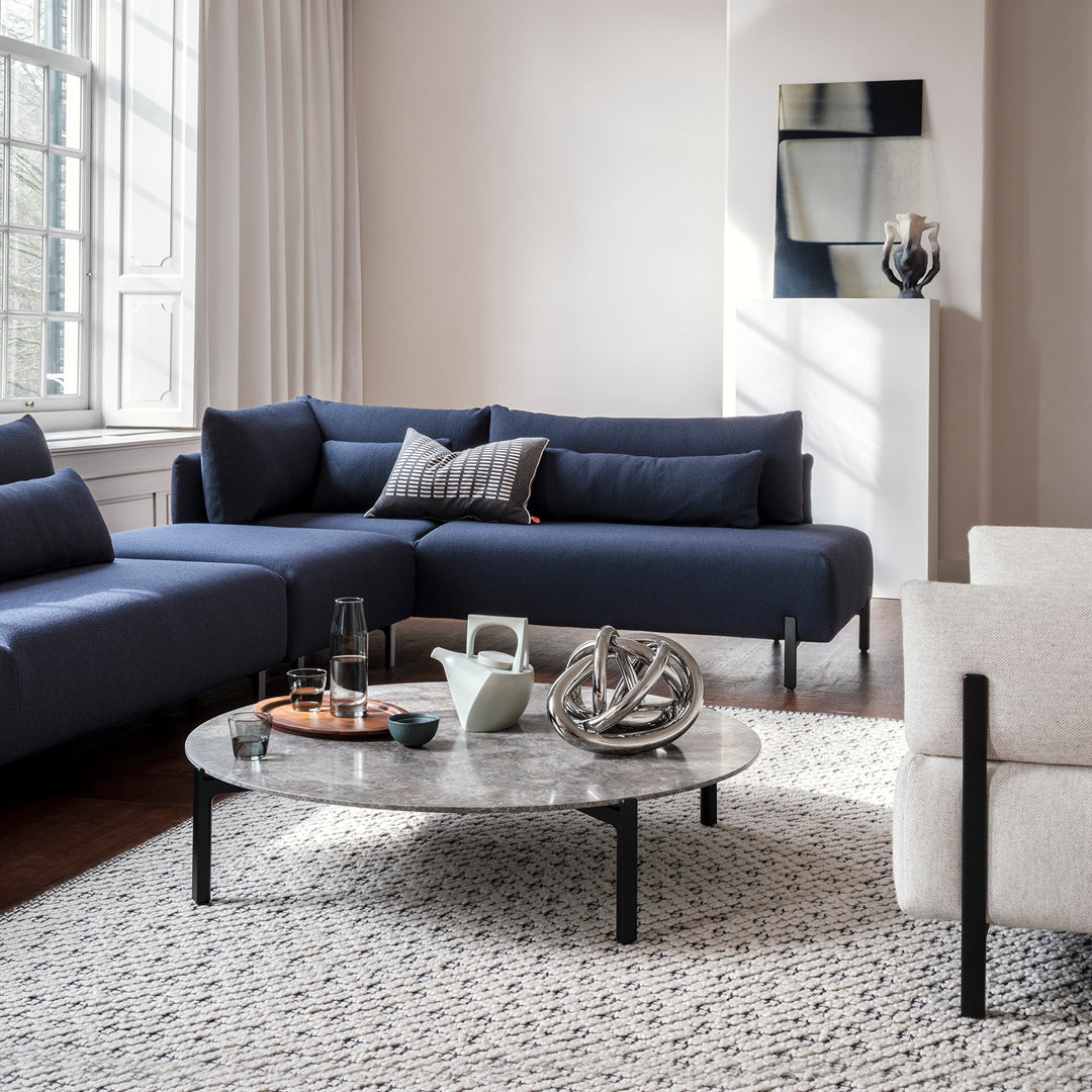 Modern navy blue sectional sofa with light gray accents, paired with a sleek round marble coffee table and patterned rug.