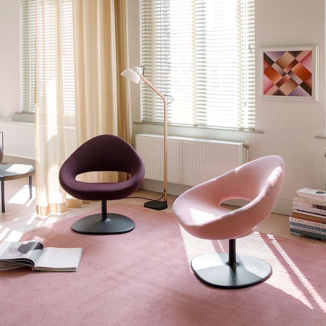 Two modern chairs: one deep purple, one soft pink, on a light pink carpet in a bright, stylish room.