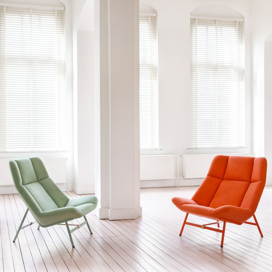 "Mint green and bright orange modern lounge chairs in a sunlit room with white walls and wooden flooring."