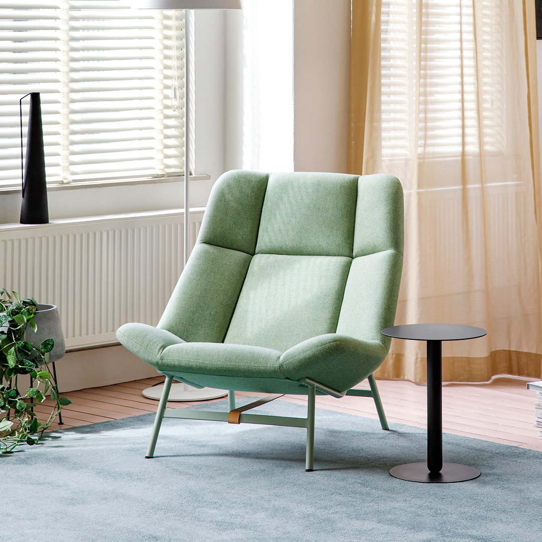 Green upholstered armchair with geometric pattern and metal legs, complemented by a black side table.