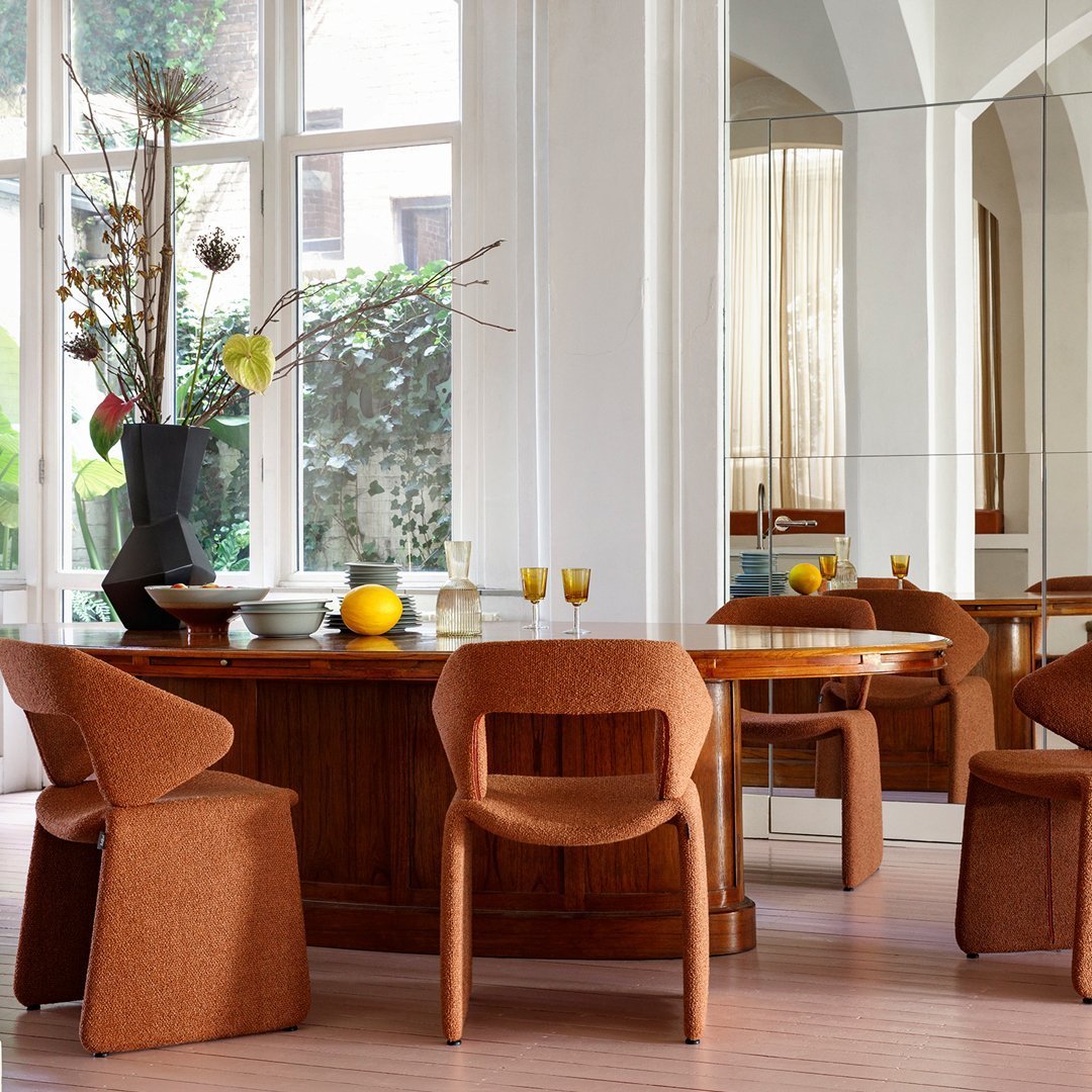 Rust-colored chairs and wooden dining table reflect warm tones in a bright, modern dining room with floral accents.