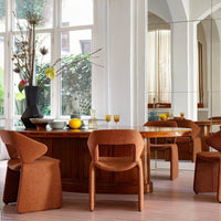 Rust-colored chairs and wooden dining table reflect warm tones in a bright, modern dining room with floral accents.
