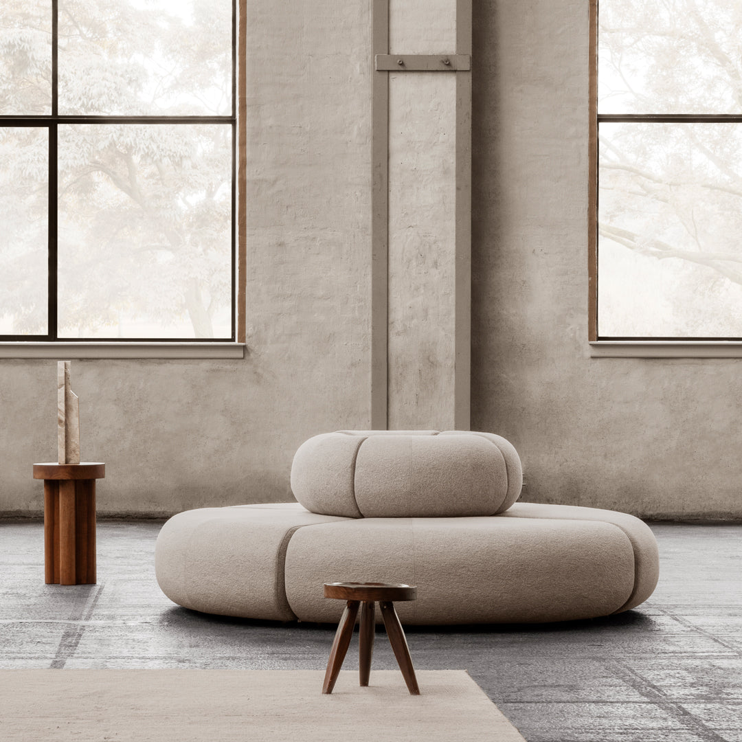 Beige circular sofa with smooth, minimalist design in a neutral-toned, modern interior setting.