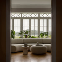 Light beige curved sofa with soft textures, paired with neutral decorative elements against a natural green backdrop.