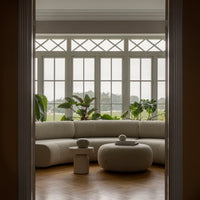 "Cozy neutral-toned sofa with round accent table, surrounded by green plants and soft natural light."