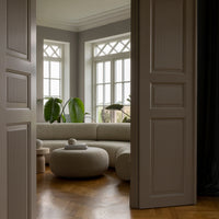 Light gray walls with subtle texture, dark wooden flooring, and a soft beige circular sofa create a warm, modern aesthetic.