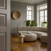 Soft beige curved sofa with a minimalist round coffee table, framed by gray walls and warm wooden flooring.