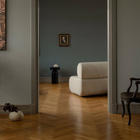 Elegant white sofa against a muted gray wall, featuring warm wooden herringbone flooring and subtle decorative elements.