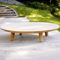 Round white tabletop with natural wood legs, set against a green outdoor backdrop, stylish and modern design.