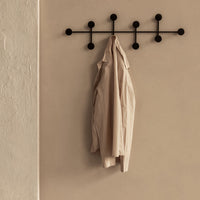 Beige lightweight jacket hanging on a black wall-mounted hook against a soft, neutral background.