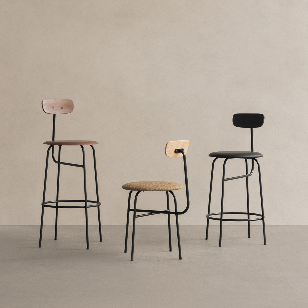 Three contemporary bar stools featuring black, wood, and beige upholstery in minimalist patterns against a neutral backdrop.