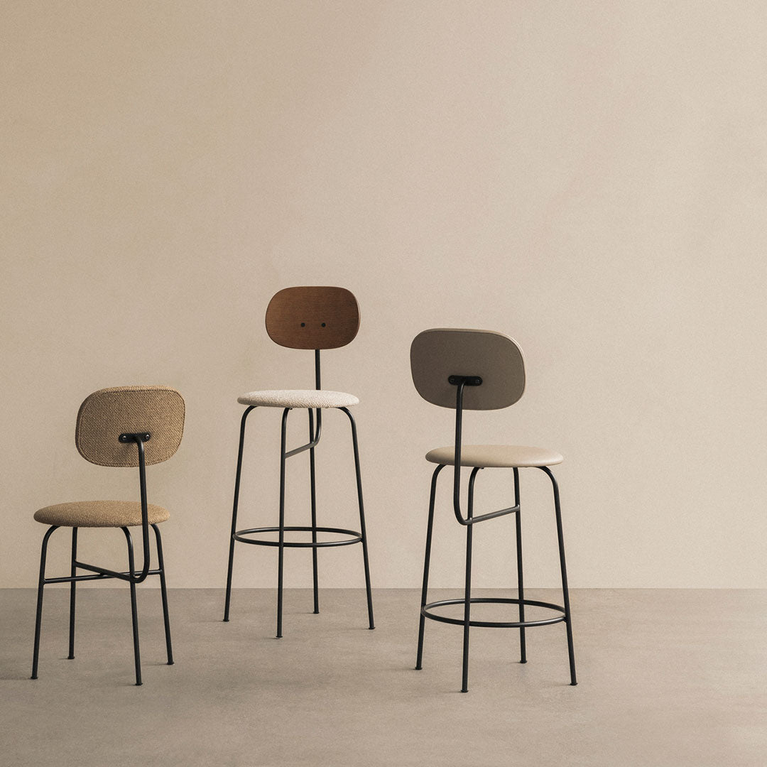 Three modern bar stools in beige, taupe, and brown hues with minimalist black metal frames against a soft beige background.