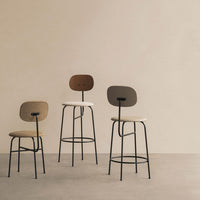 Three modern bar stools in beige, taupe, and brown hues with minimalist black metal frames against a soft beige background.