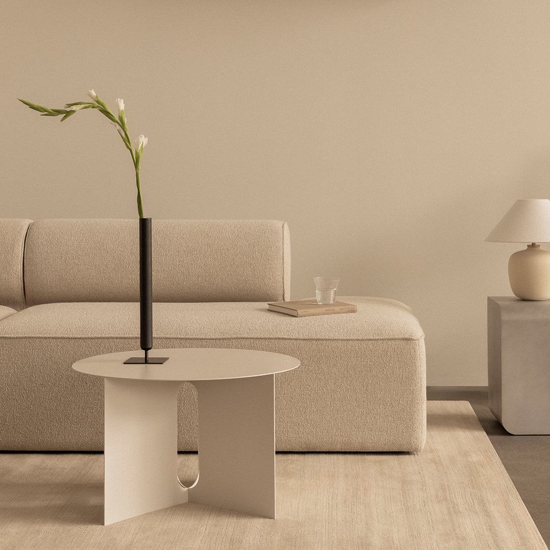 Minimalist beige and cream living space featuring a sleek round table and soft, textured sofa. Modern, neutral tones.
