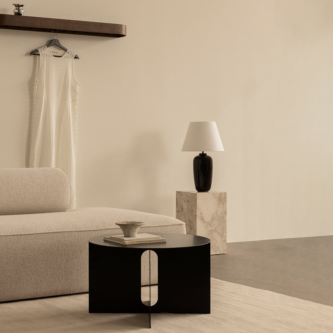Black round coffee table with modern design, complemented by soft beige tones and minimalist patterns in the room.