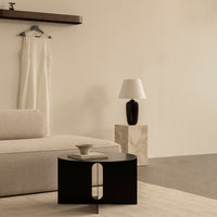 Black round coffee table with a minimalist design, set against soft beige walls and light neutral furnishings.