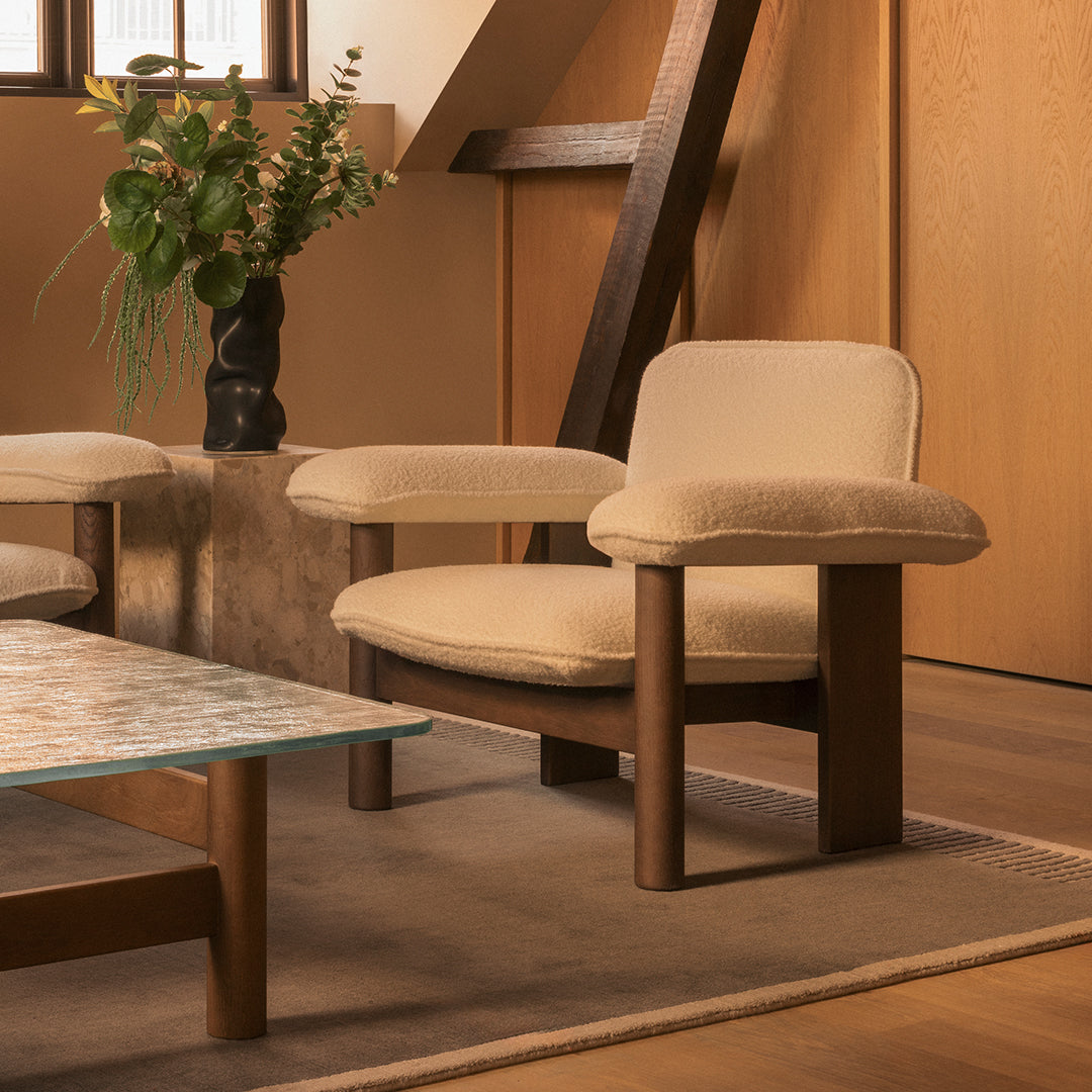 Beige upholstered chair with a wood frame, set in a warm-toned room with minimalist decor and earthy plant accents.