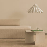 Beige textured sofa, cream sculptural lamp, and round white table with green book, creating a soft, minimalist palette.
