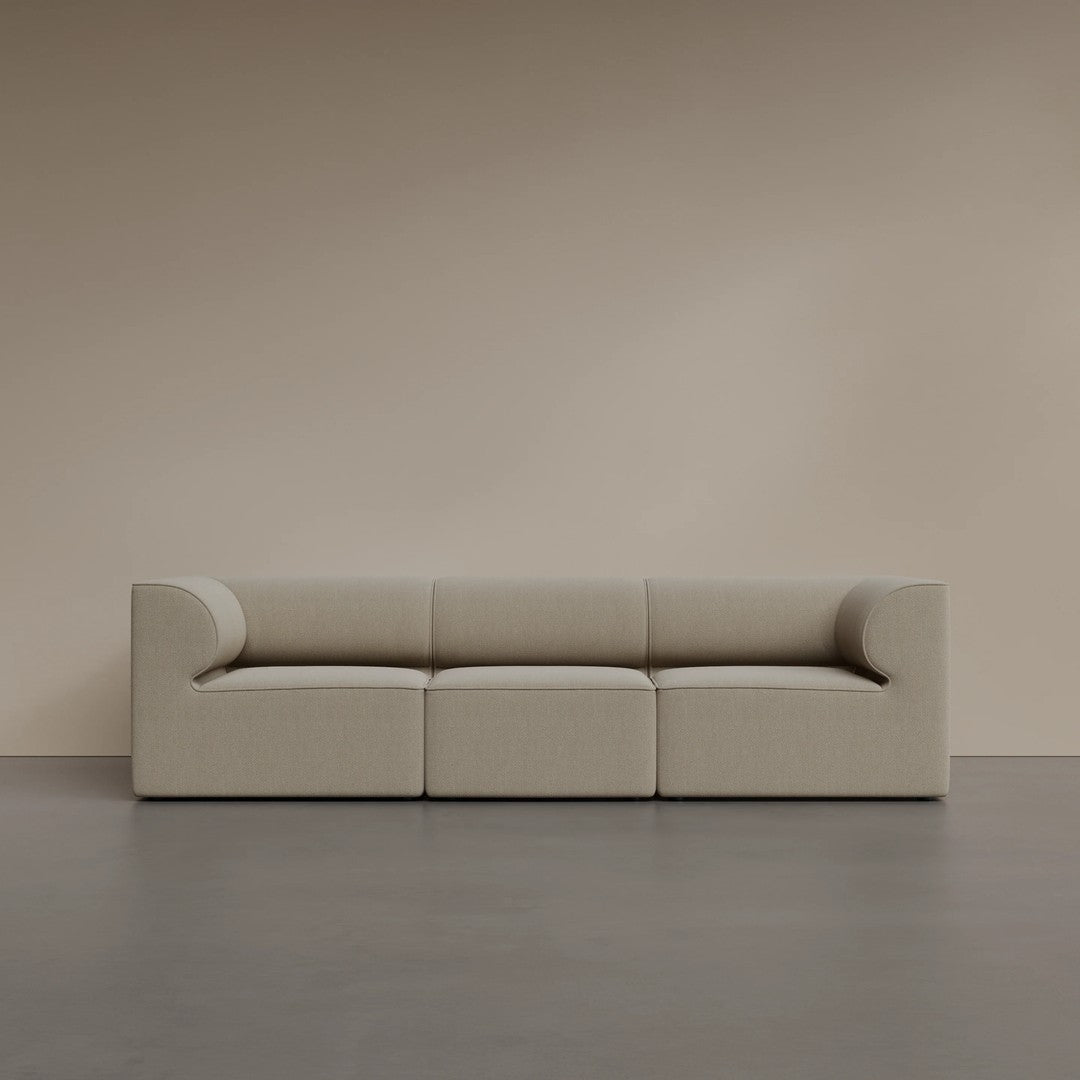 Beige minimalist sofa with soft, curved lines against a warm-toned wall and smooth gray floor.