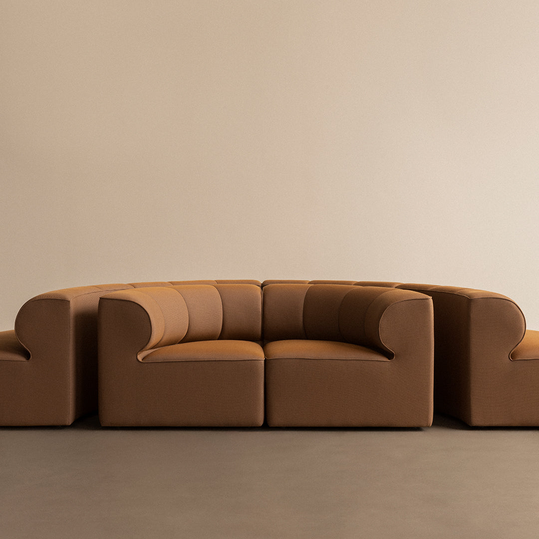 Curved sofa in rich tan upholstery with smooth, rounded edges and subtle vertical patterns for a modern look.