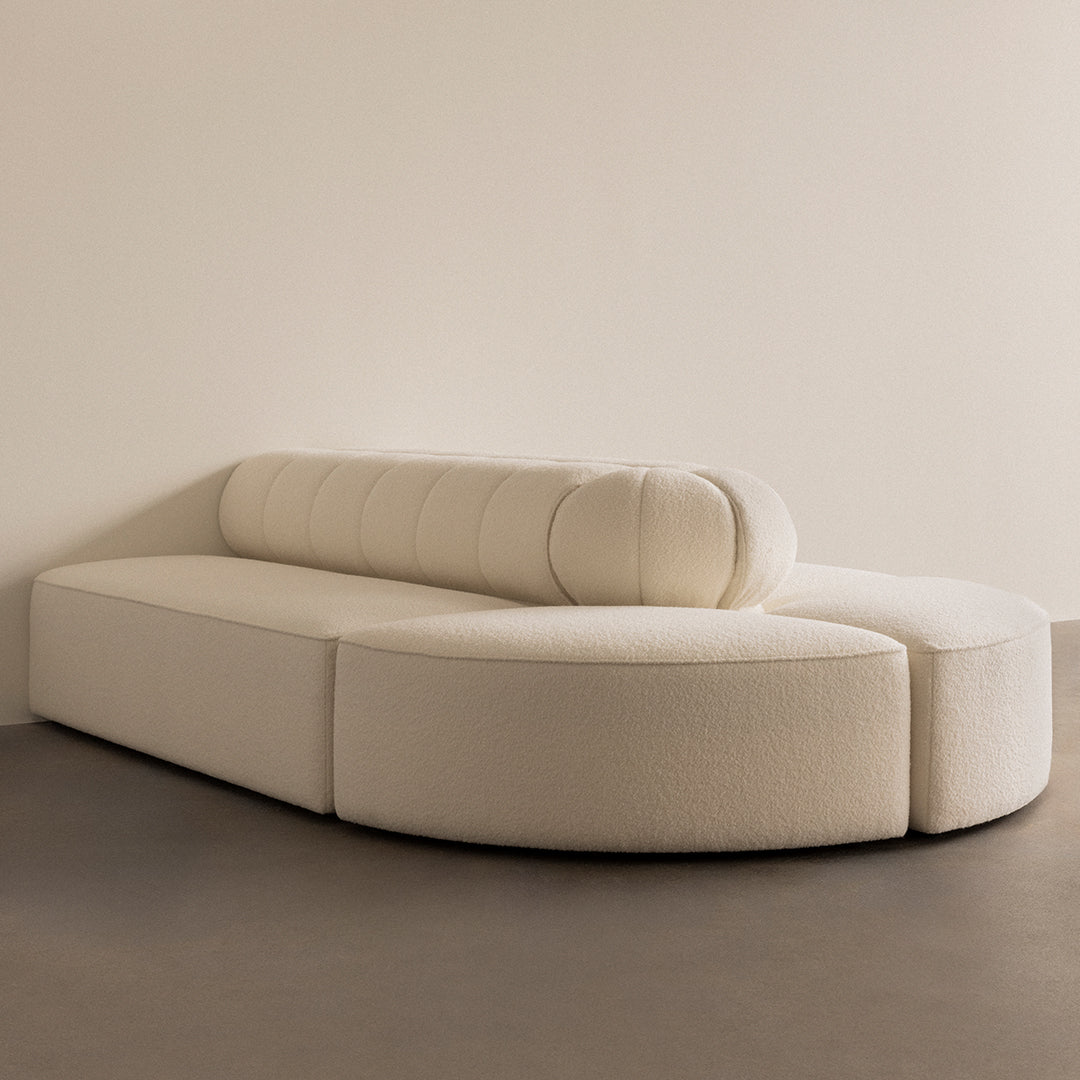 Cream-colored curved sectional sofa with soft, textured upholstery and round bolster cushions, perfect for modern decor.