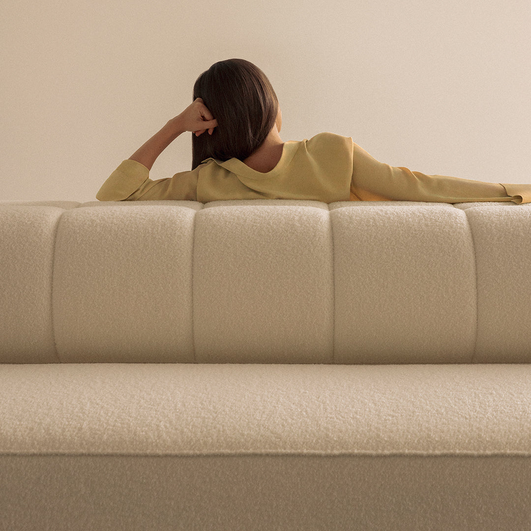 Soft cream-colored sofa with subtle texture against a pale background, featuring minimalist design and gentle curves.