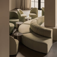 Curved green fabric seating arrangement with soft textures and subtle tones, complemented by sleek side tables.