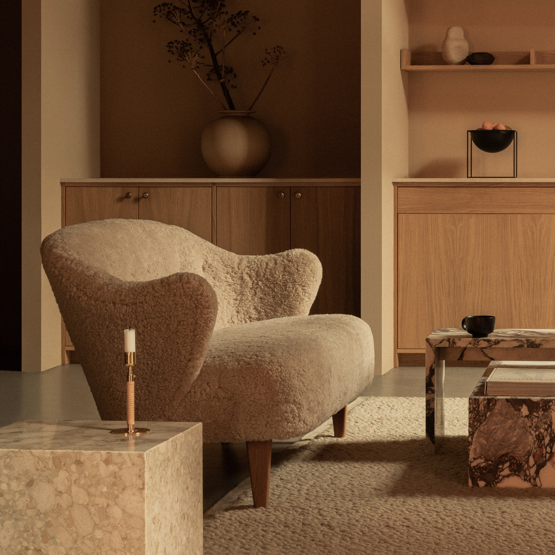 Beige upholstered armchair with a curved silhouette, complemented by a textured, soft fabric against a warm-toned background.