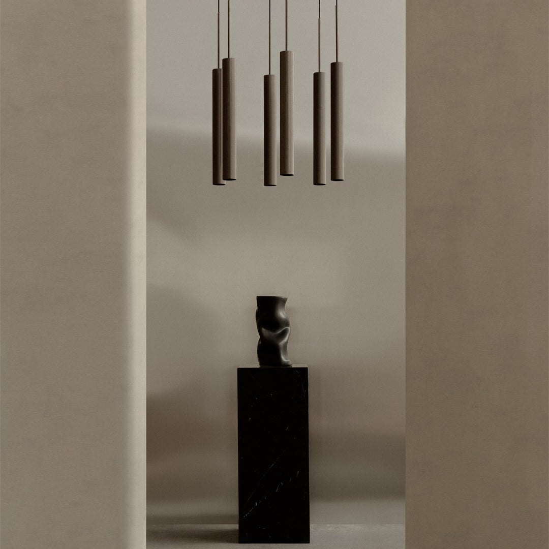 Sleek black pedestal with a textured dark vase, complemented by subtle earthy tones and elegant brown hanging lights.