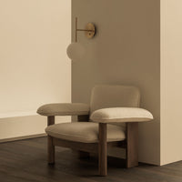 Soft beige armchair with plush upholstery and warm wooden legs, complemented by a light beige wall and smooth brown flooring.