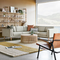 Light gray sectional sofa, beige and yellow patterned rug, wooden round table, and warm brown accents in a modern room.