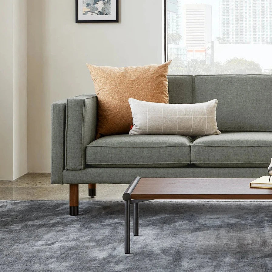 Green sofa with textured cushions in orange and cream, set on a gray patterned rug, enhancing modern decor.
