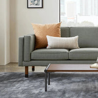 Green sofa with textured cushions in orange and cream, set on a gray patterned rug, enhancing modern decor.