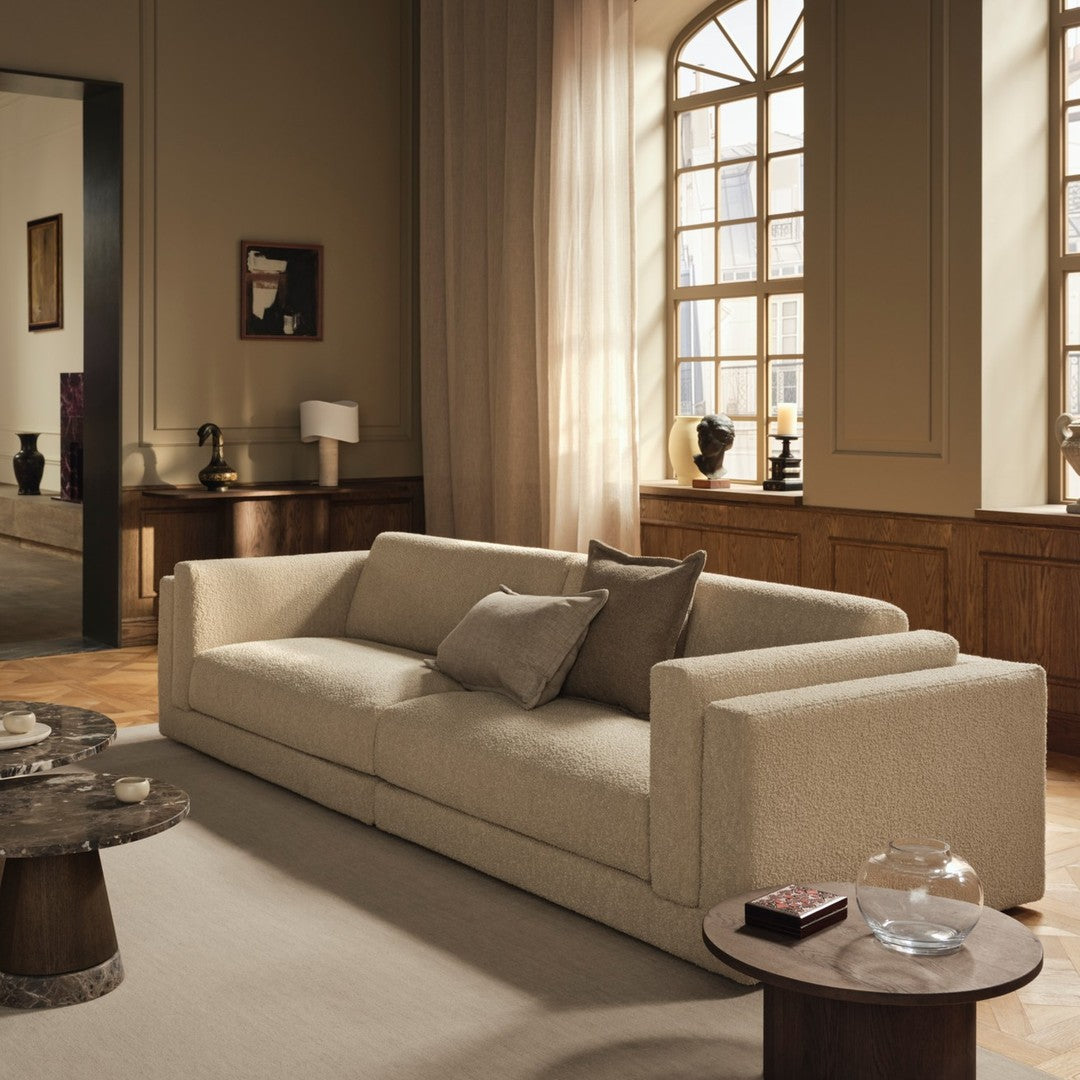 Beige sofa with smooth, modern lines and two accent pillows, set against a soft, neutral-toned interior.